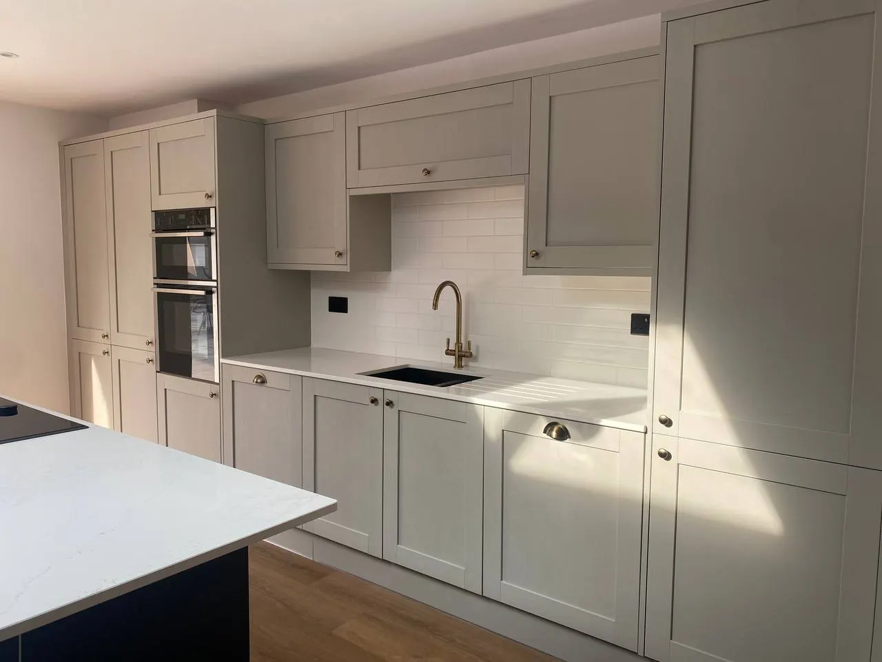 Greige perimeter units with an integrated double oven and quartz splashback